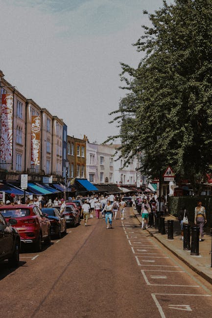 The exterior of Notting Hill Garage, a small multi-storey building with a dark green facade, is shown in this image. A vintage silver car is parked on the cobblestone pavement directly in front of the